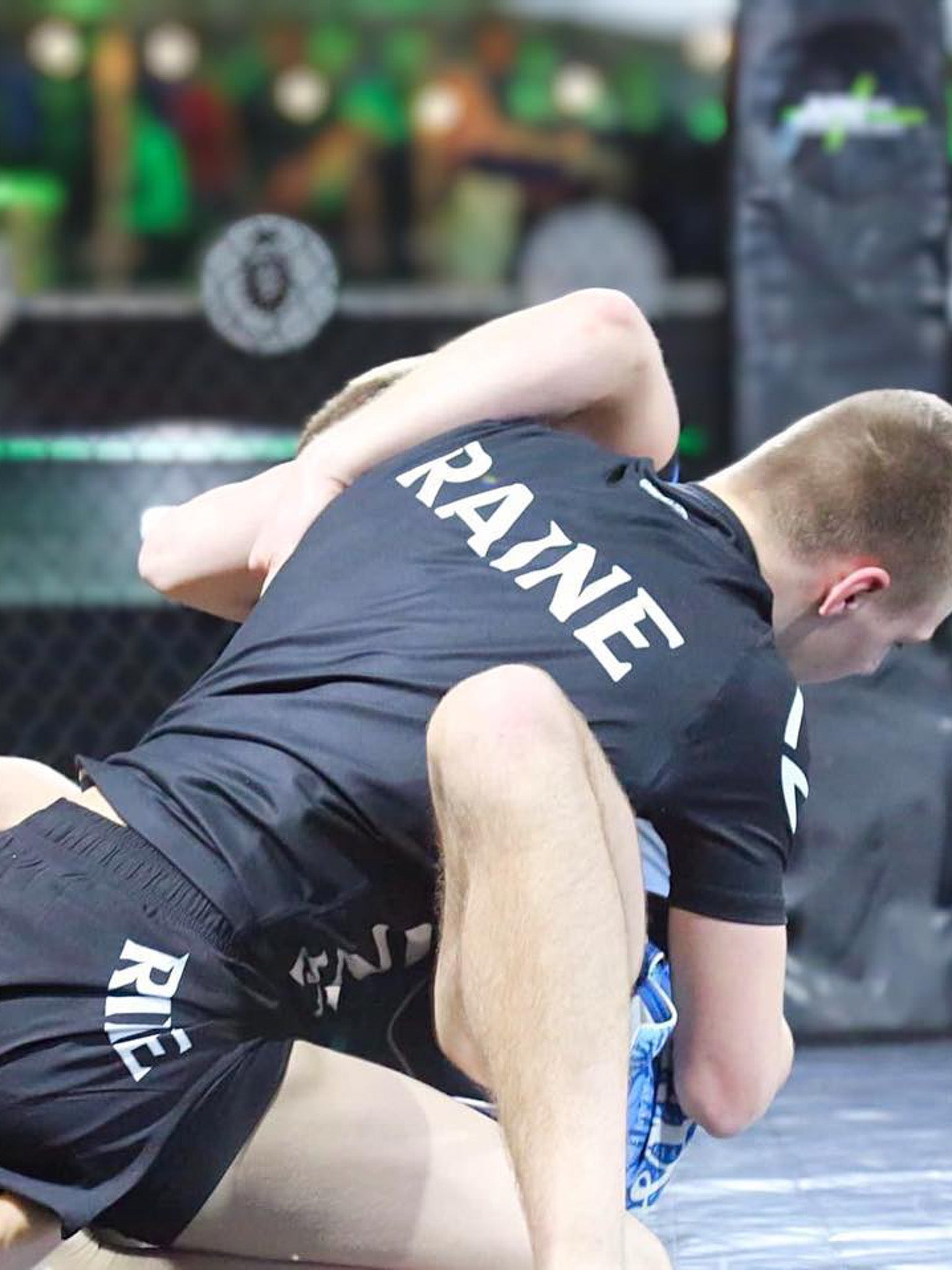 Two individuals in black athletic wear with 'RAINE' branding on a blurred background