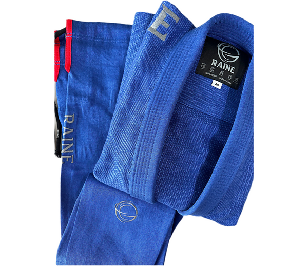 A blue Brazilian jiu-jitsu gi with the RAINE brand logo on the shoulders and a red drawcord.
