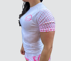 A woman wearing a white and pink BJJ rash guard with short, pink polka-dotted sleeves.