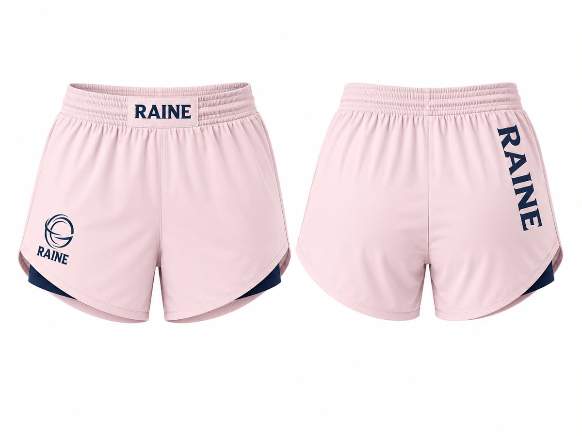 Front and back views of light pink athletic shorts with navy blue accents, featuring the word 'RAINE' printed on the waistband and down the left leg, with a circular logo on the right leg.