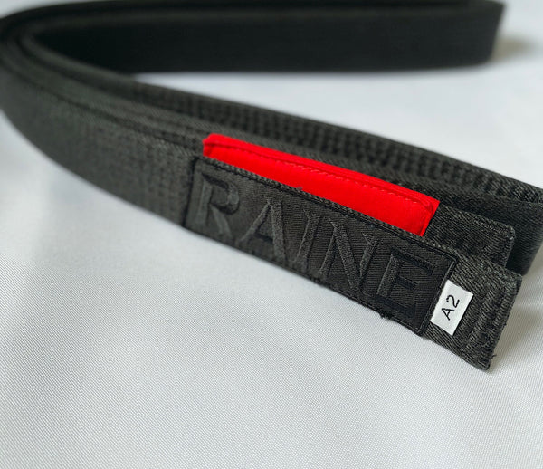 A black hemp BJJ belt with a red patch showing the brand name 'RAINE' and a size label 'A2'.