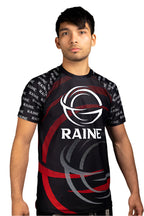 A man wearing a black and red short-sleeved BJJ rash guard with the brand logo 'RAINE' featured prominently