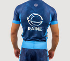 Back of a man wearing a blue Peruse BJJ rash guard with short sleeves and RAINE branding.